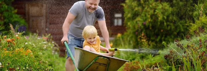 Person schiebt Kind in Schubkarre durch Garten